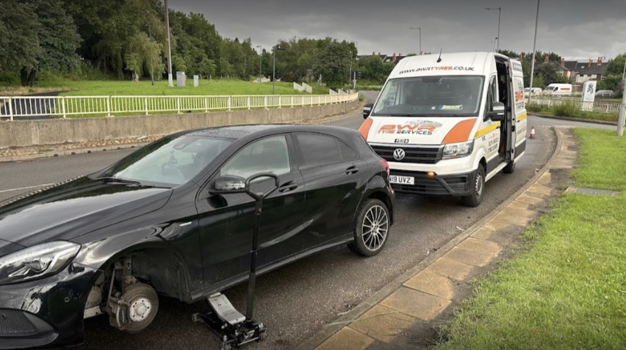 Mobile tyre fitting technician changing a tyre on a modern vehicle with a white Sprinter van in the background on a Bradford street