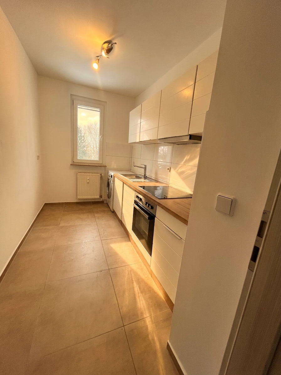 Sanierte Küche mit weißen Hochglanzfronten, Holzarbeitsplatte, Einbauofen und Fliesenboden – 3-Zimmer-Wohnung in Schorfheide
