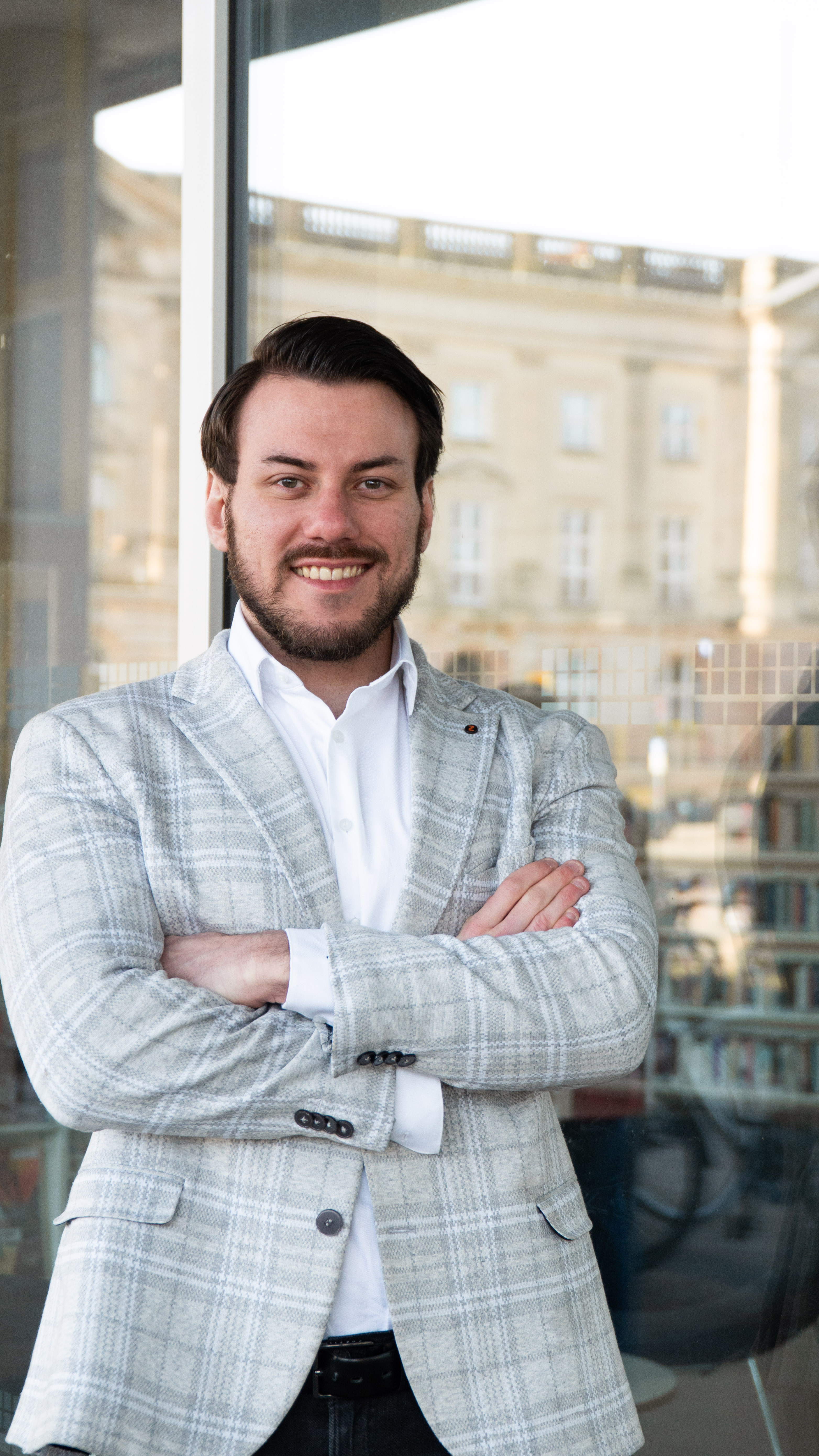 Daniel Schaposch, Gründer und Hausverwalter von Bester Vermieter, lächelnd vor einem Glasfenster mit Stadtblick