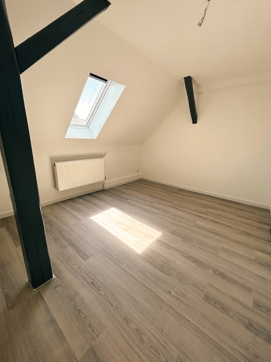 Helles Dachgeschosszimmer mit dunklem Holzbalken, Dachfenster und grauem Laminatboden – Dessau