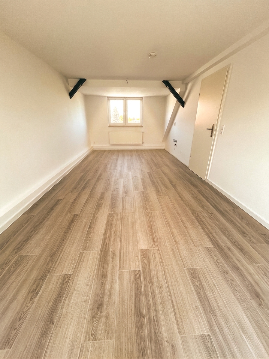 Weiteres helles Zimmer mit Dachschräge, Holzbalken und hellem Laminatboden – Dachgeschosswohnung Dessau