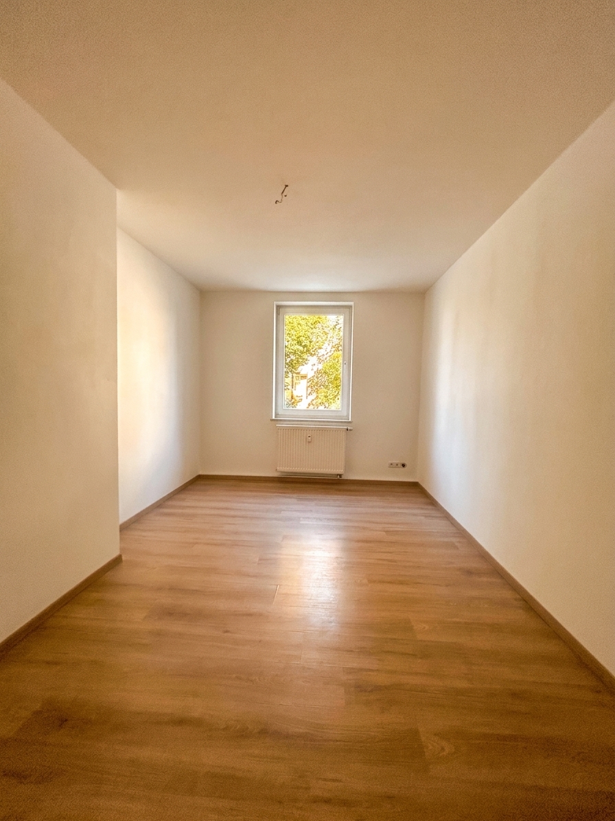 Helles Zimmer mit warmem Laminatboden und Fenster mit Gartenblick – 4-Zimmer-Wohnung in Dessau-Roßlau