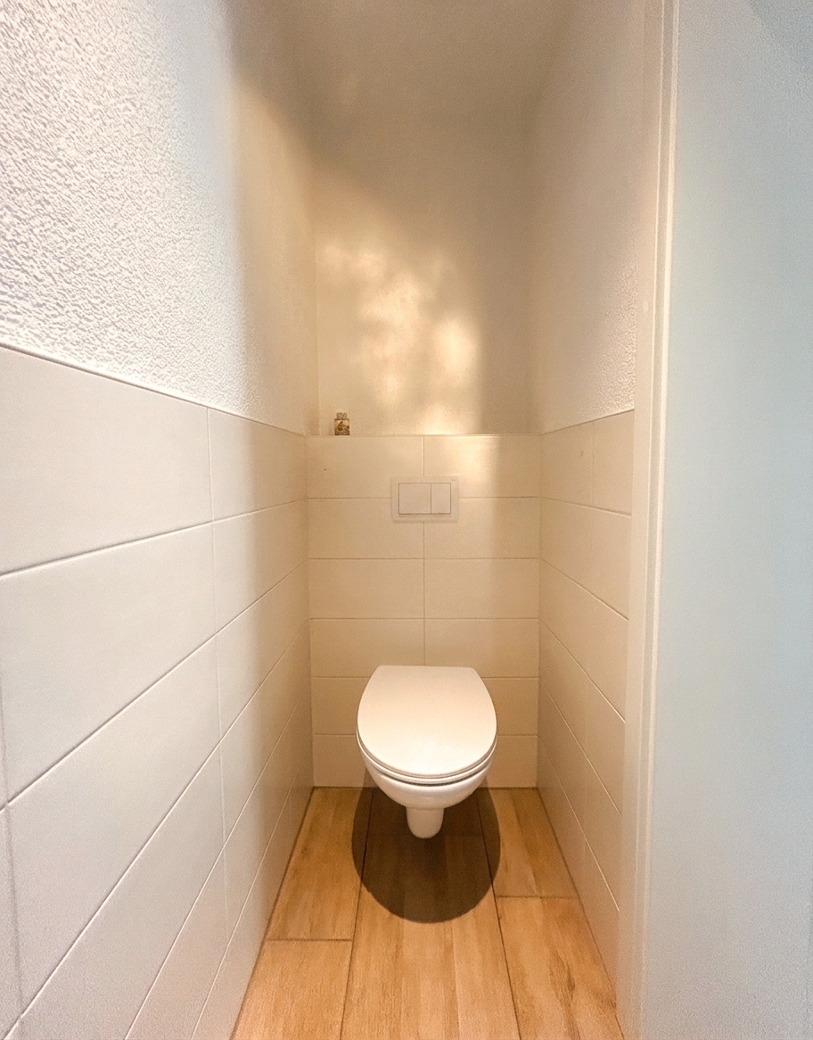 Separates WC mit wandhängendem Toilette, weißen Fliesen und Holzboden – 4-Zimmer-Wohnung in Dessau-Roßlau