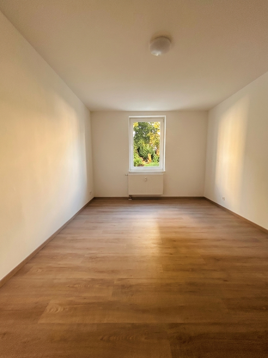 Helles Zimmer mit Fenster und Gartenblick, warmem Laminatboden und weißen Wänden – 4-Zimmer-Wohnung in Dessau-Roßlau