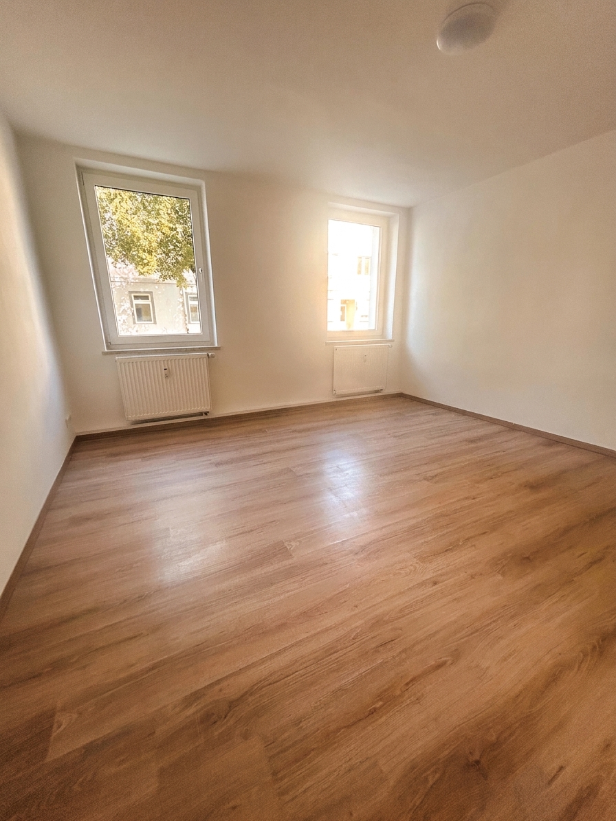 Helles Zimmer mit zwei Fenstern, warmem Laminatboden und weißen Wänden – 4-Zimmer-Wohnung in Dessau-Roßlau