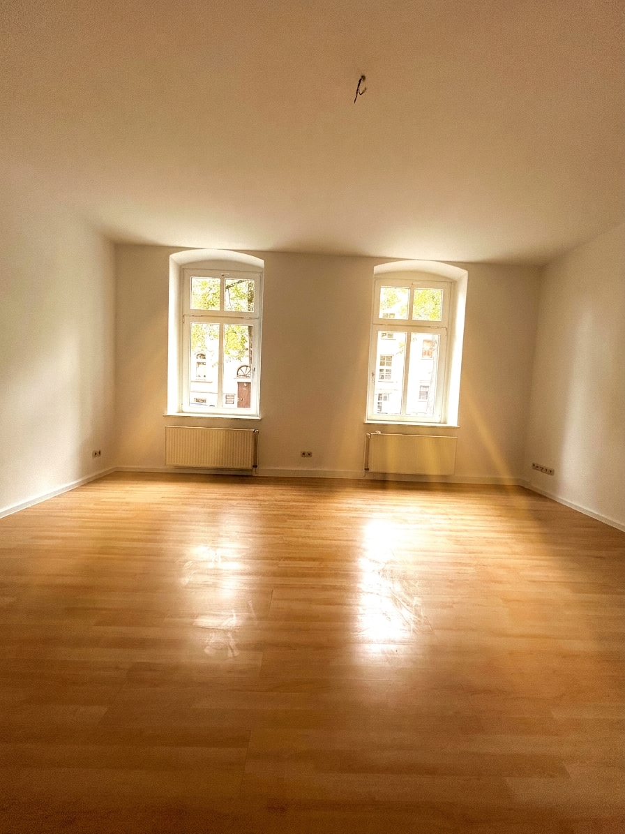 Großes, lichtdurchflutetes Wohnzimmer mit zwei Bogenfenstern und warmem Holzboden – 3-Zimmer-Wohnung in Dessau-Roßlau
