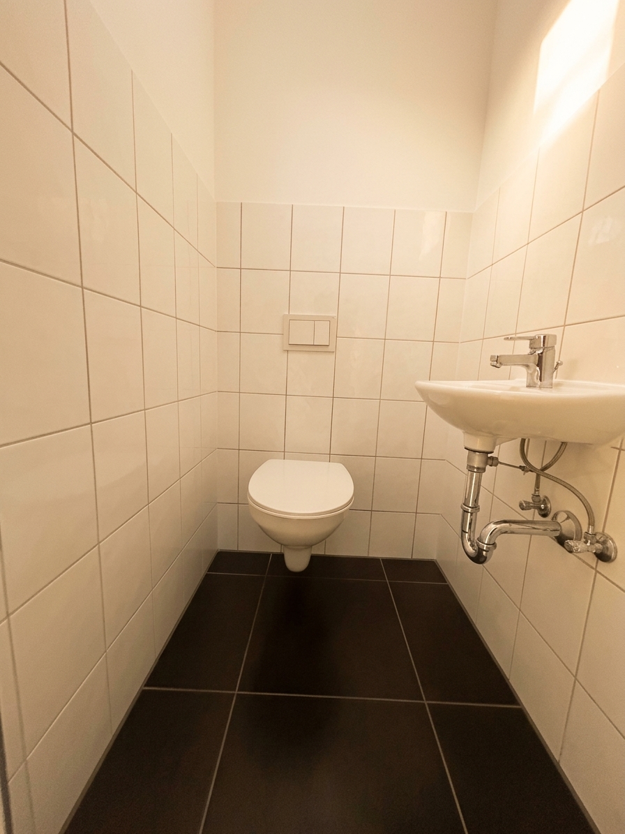 Gäste-WC mit wandhängendem WC, kleinem Waschbecken und dunklem Fliesenboden – 4-Zimmer-Wohnung in Dessau-Roßlau