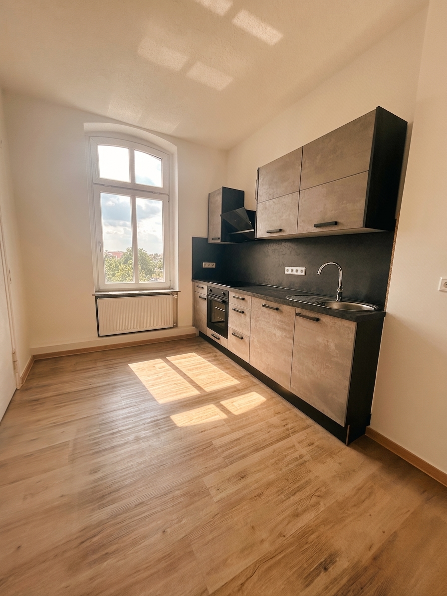 Moderne Küche mit dunklen Fronten, schwarzer Arbeitsplatte, Einbauofen und Bogenfenster – 3-Zimmer-Wohnung in Dessau-Roßlau
