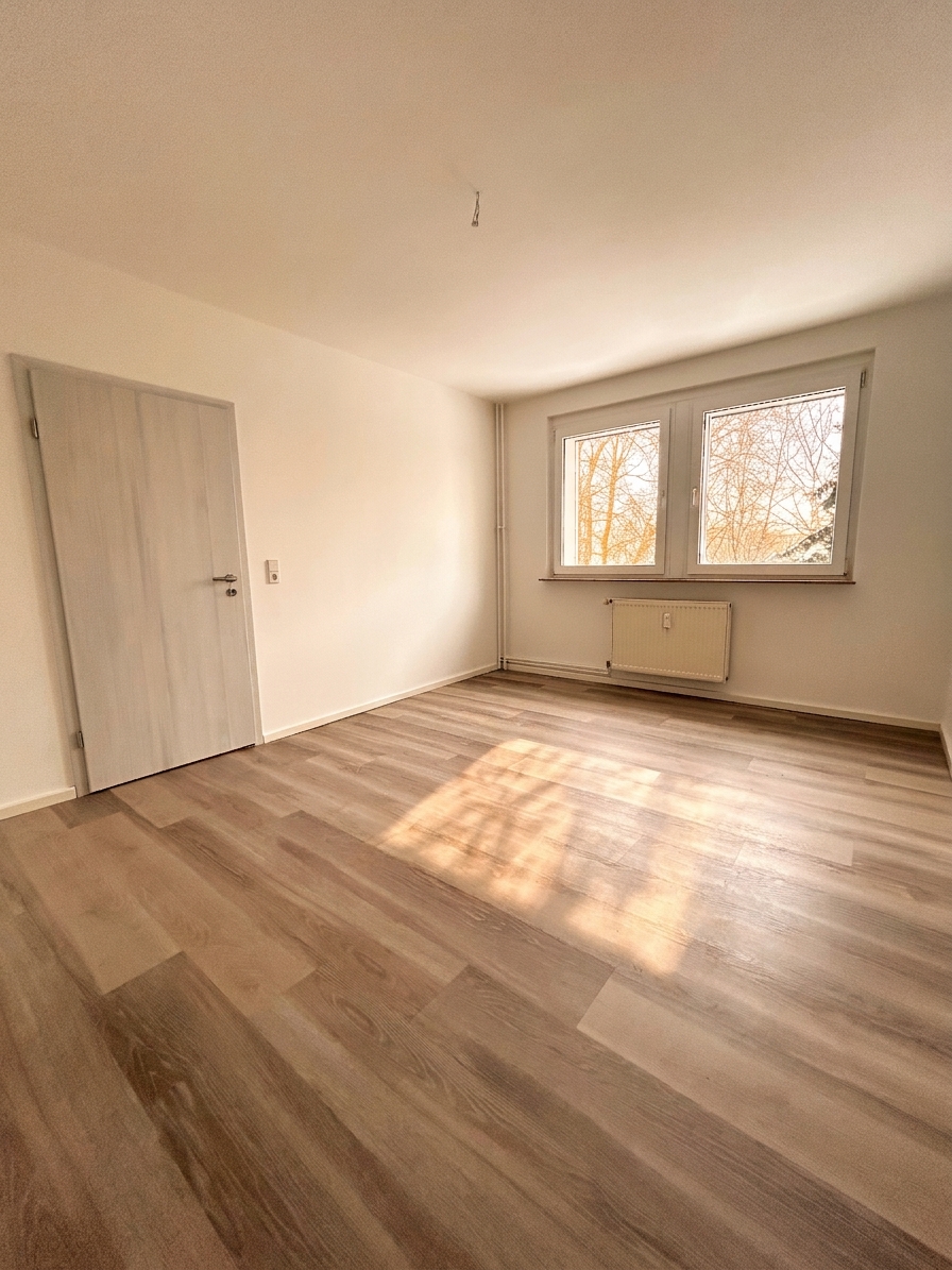 Helles Schlafzimmer mit warmem Laminatboden, weißen Wänden und Fenster mit Baumblick – 3-Zimmer-Wohnung in Schorfheide