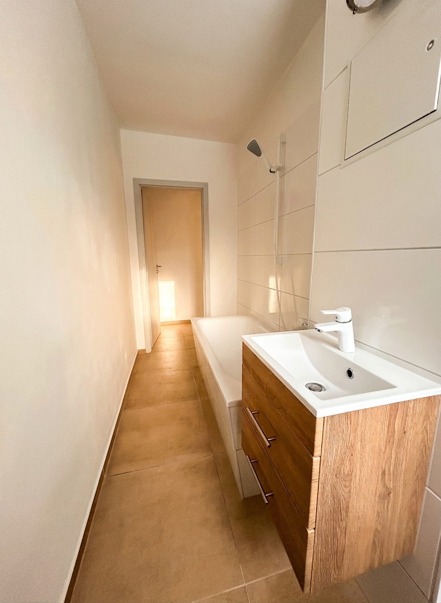 Badezimmer mit Waschtisch, Holzunterschrank, Badewanne und Spiegel – 3-Zimmer-Wohnung in Schorfheide