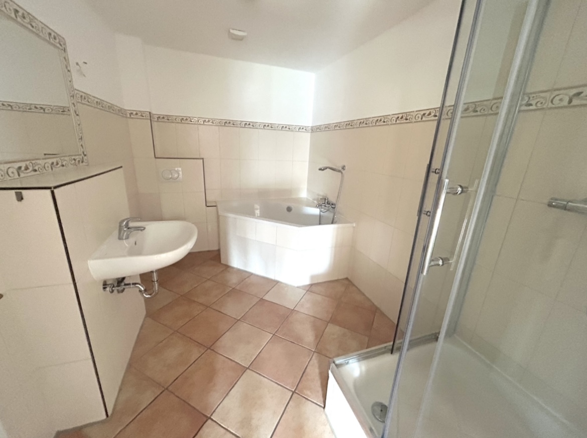 Badezimmer mit Eckbadewanne, Glasdusche, Waschtisch und Fliesenboden – 3-Zimmer-Wohnung in Ketzin