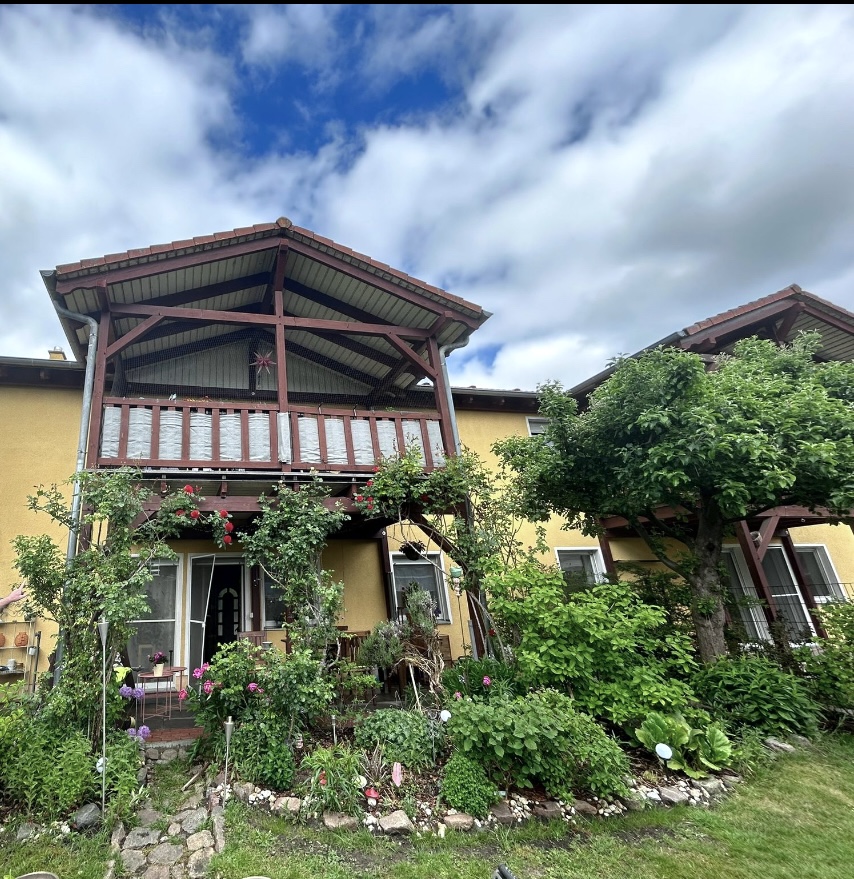 Außenansicht des Hauses mit überdachtem Balkon, Garten und blühendem Vorgarten – 3-Zimmer-Wohnung in Ketzin