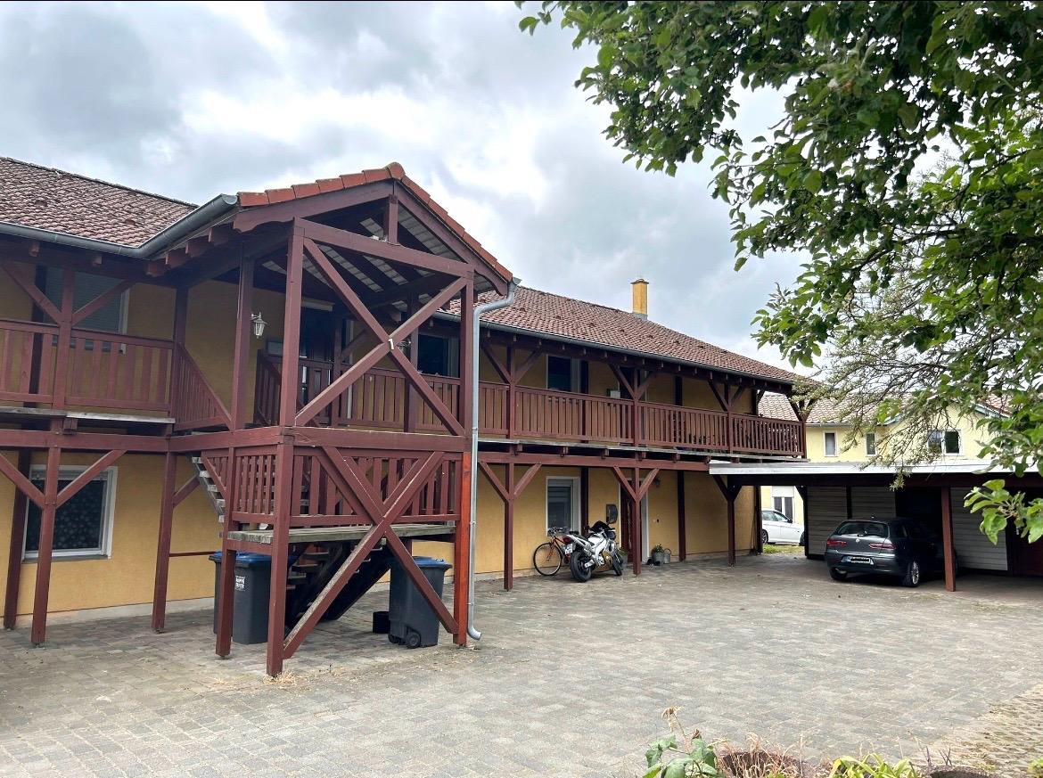 Außenansicht des Hauses mit überdachtem Balkon, Carport und gepflastertem Innenhof – 3-Zimmer-Wohnung in Ketzin