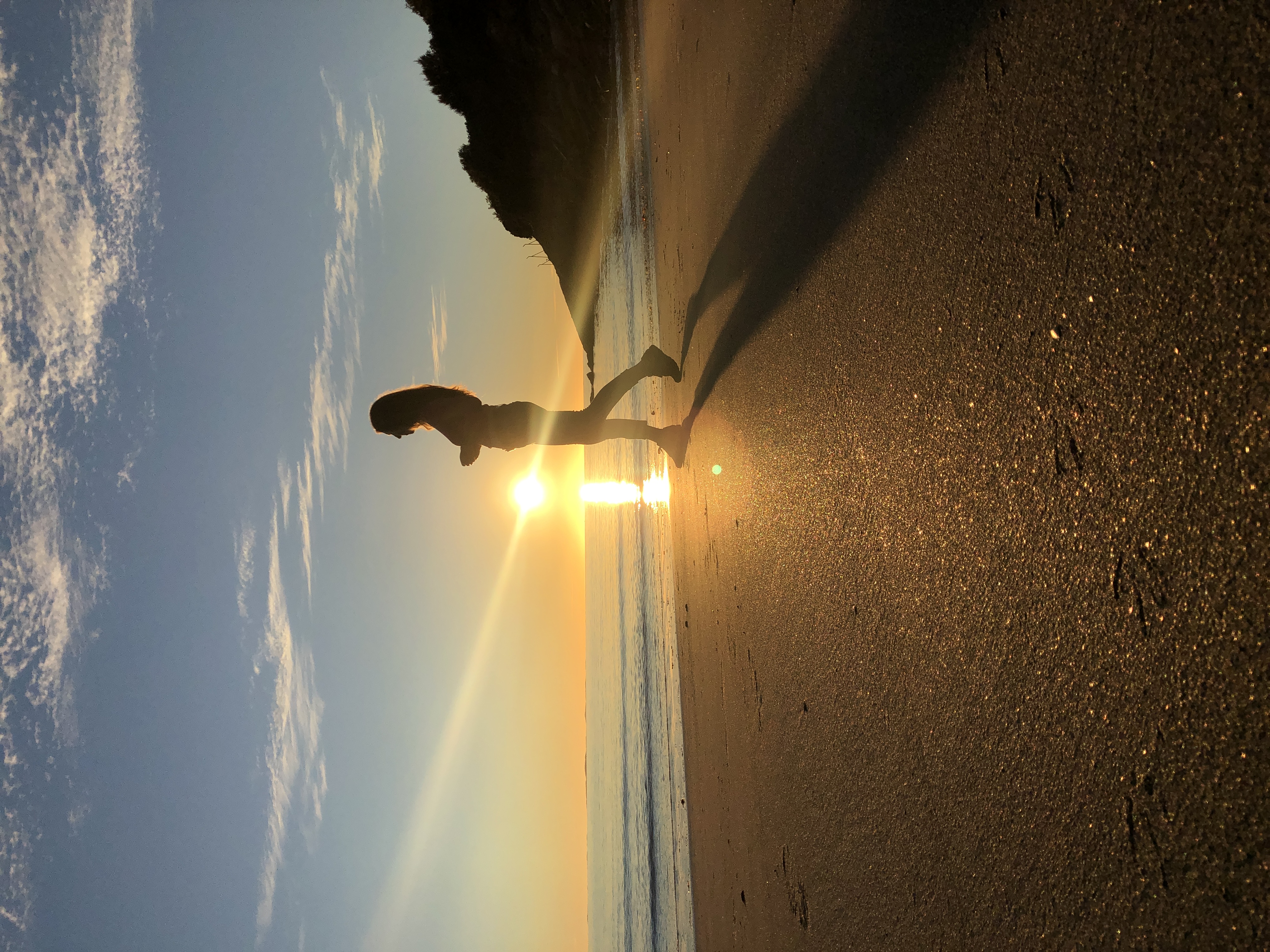 Silhuett av en kvinne som gjør en håndstand på en sandstrand i solnedgang, med gyllen solstråle og hav i bakgrunnen