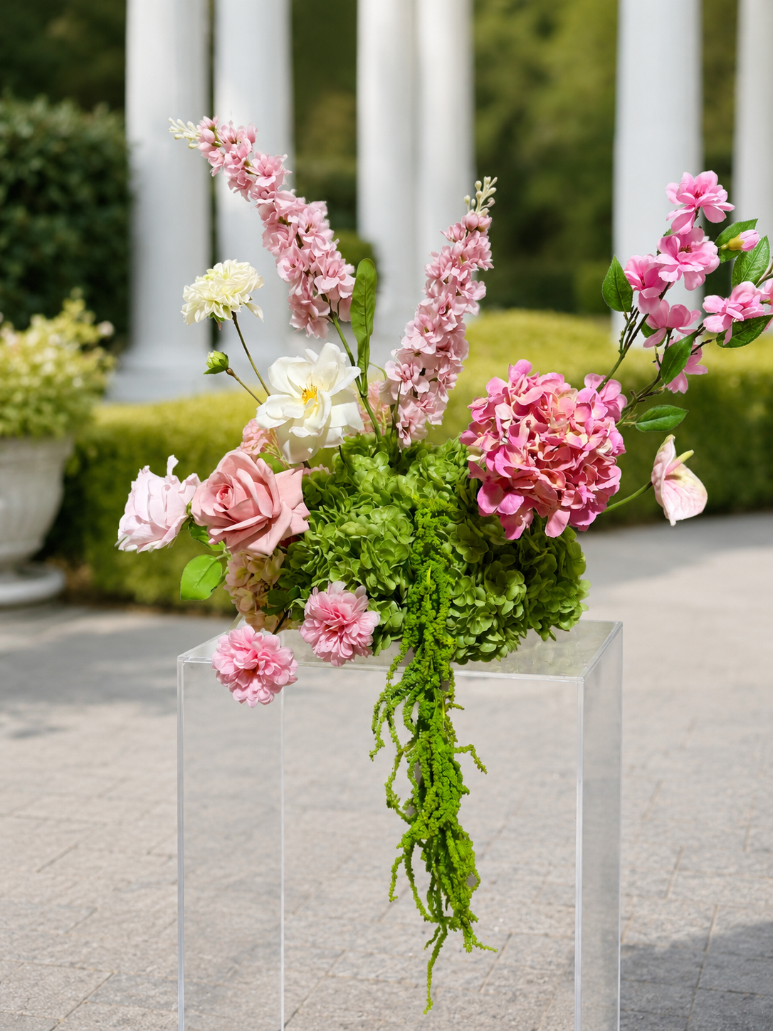 Pink floral arrangement on acrylic pedestal in garden setting